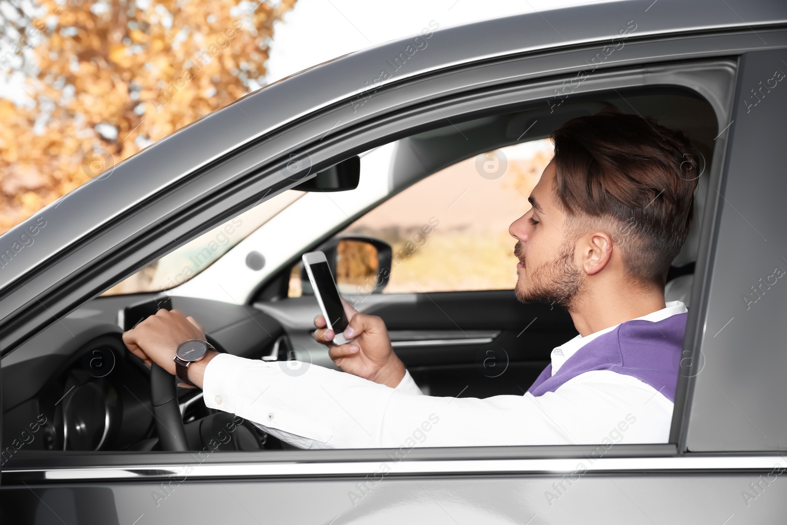 Photo of Young man using phone in driver's seat of modern car