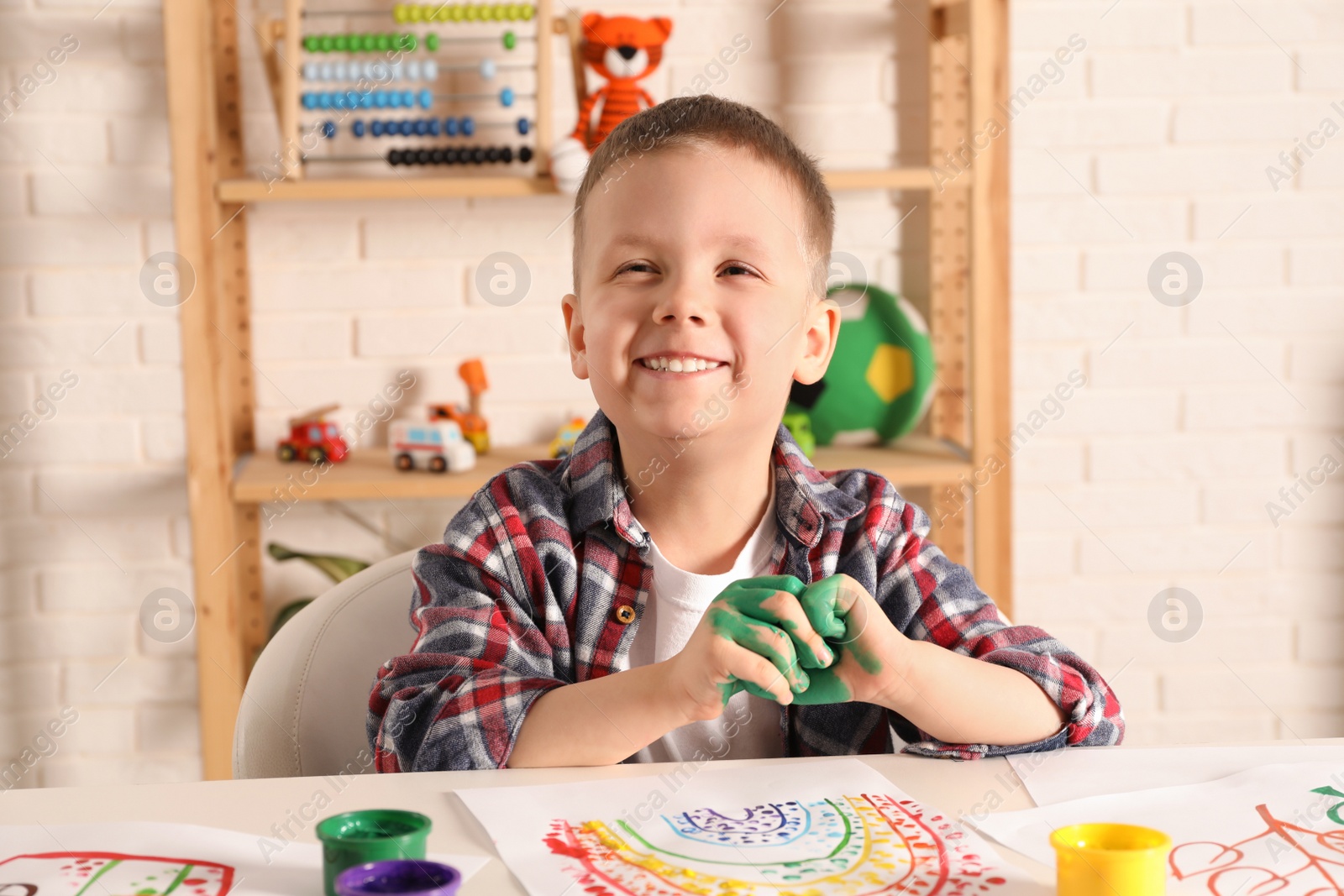 Photo of Little boy painting with fingers at white table indoors