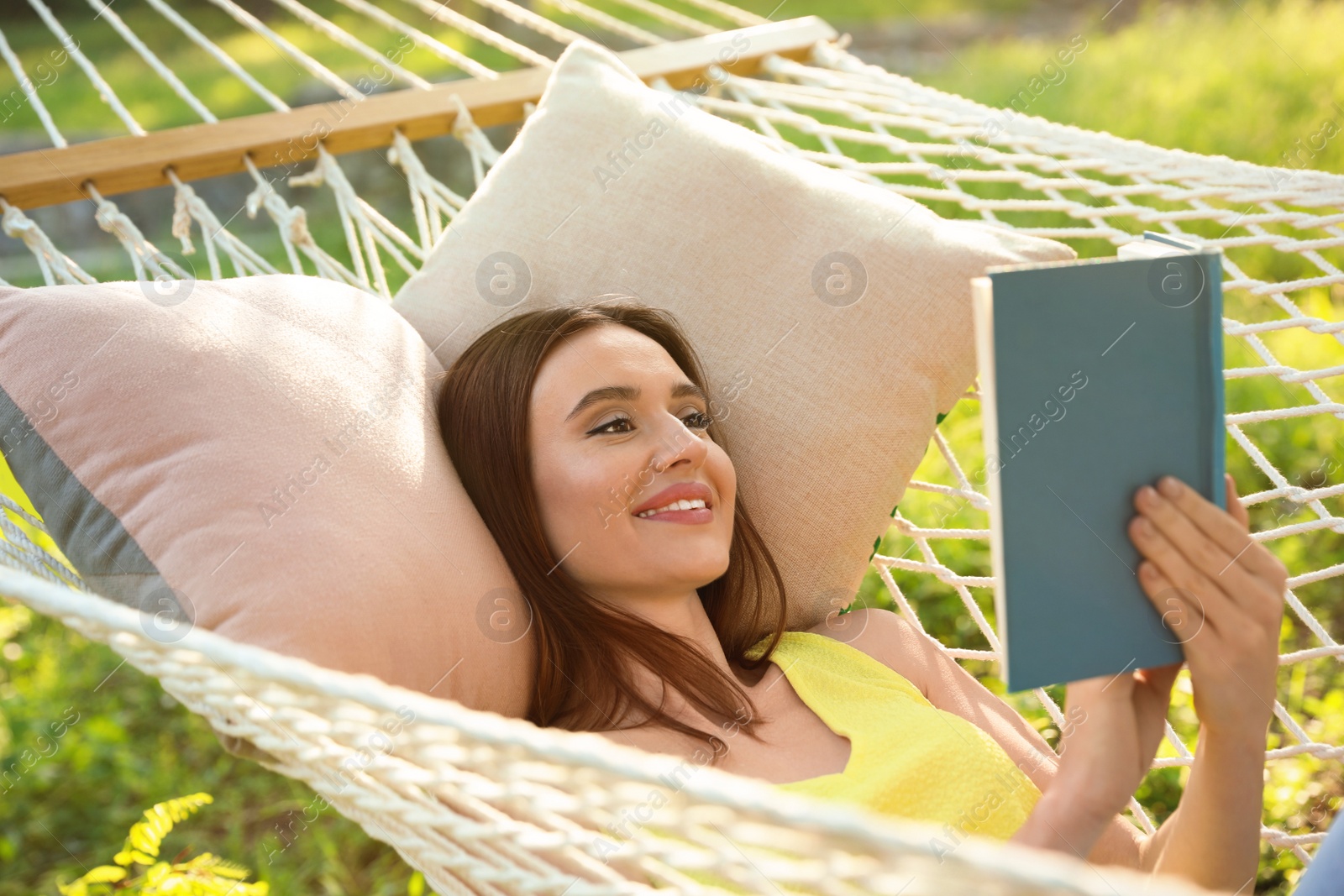 Photo of Young woman reading book in comfortable hammock at green garden