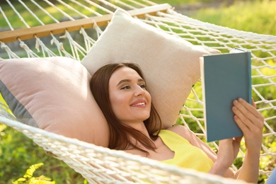 Young woman reading book in comfortable hammock at green garden