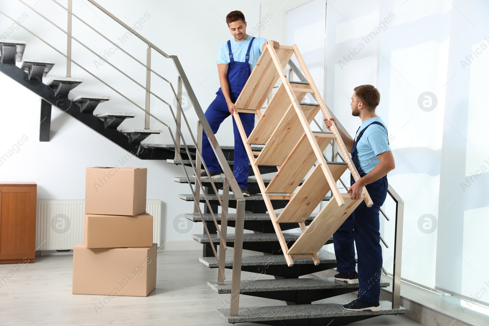 Photo of Professional workers carrying wooden rack on stairs in office. Moving service