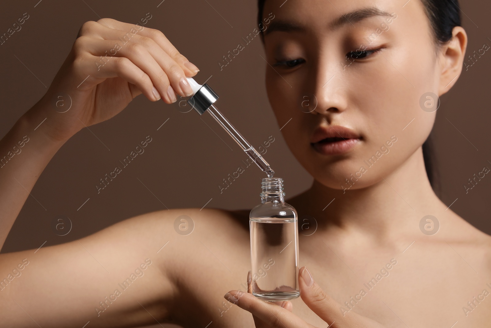 Photo of Beautiful young woman with bottle of cosmetic serum on brown background, closeup