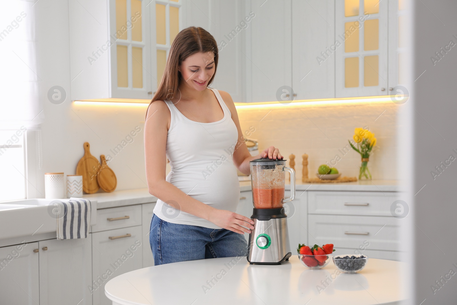 Photo of Young pregnant woman preparing smoothie at table in kitchen. Healthy eating