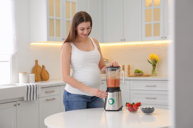 Young pregnant woman preparing smoothie at table in kitchen. Healthy eating