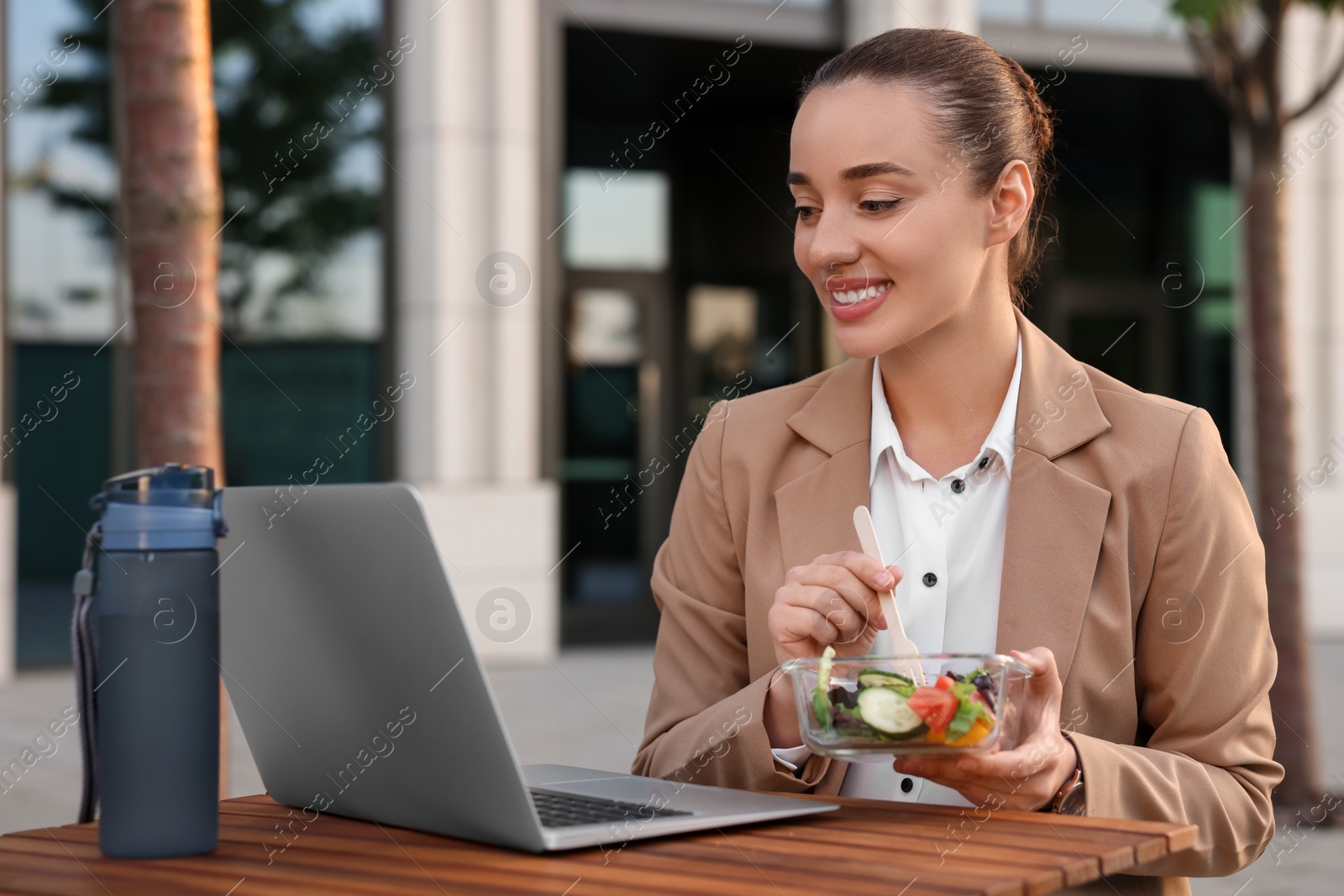 Photo of Happy businesswoman using laptop during lunch at wooden table outdoors