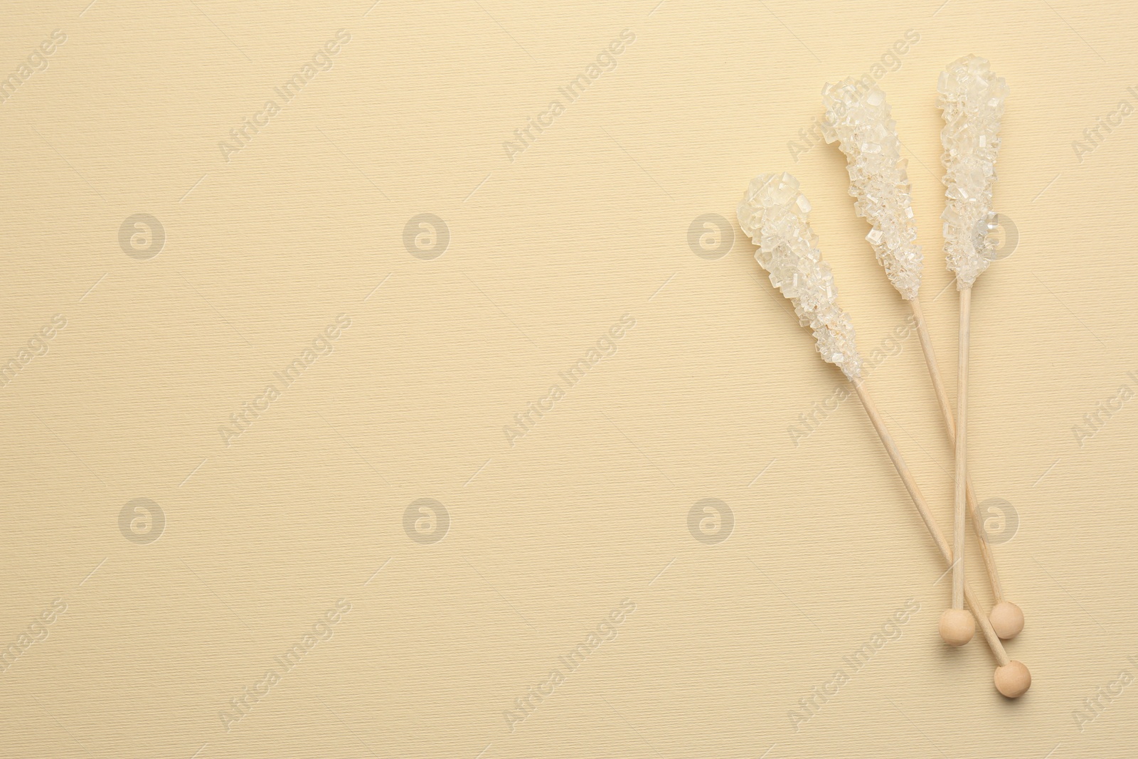 Photo of Wooden sticks with sugar crystals and space for text on beige background, flat lay. Tasty rock candies