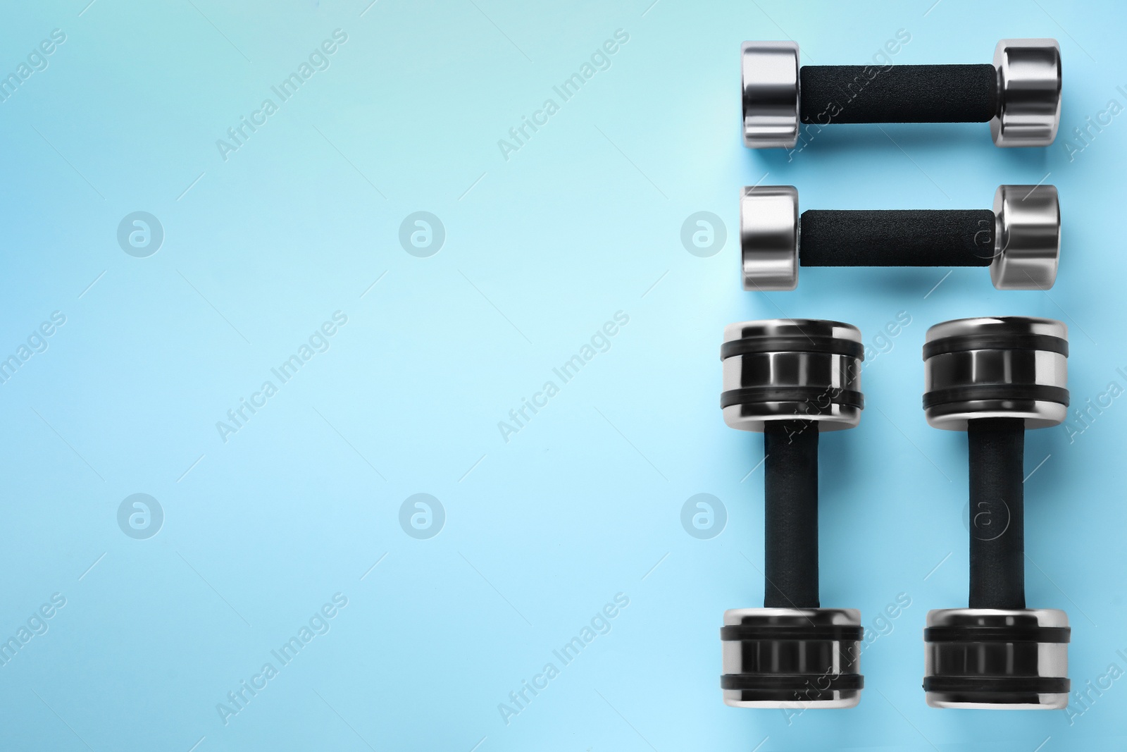 Photo of Many stylish dumbbells on light blue background, flat lay. Space for text