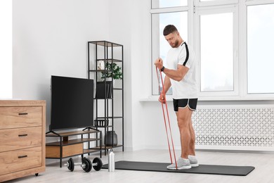 Athletic man doing exercise with elastic resistance band on mat at home