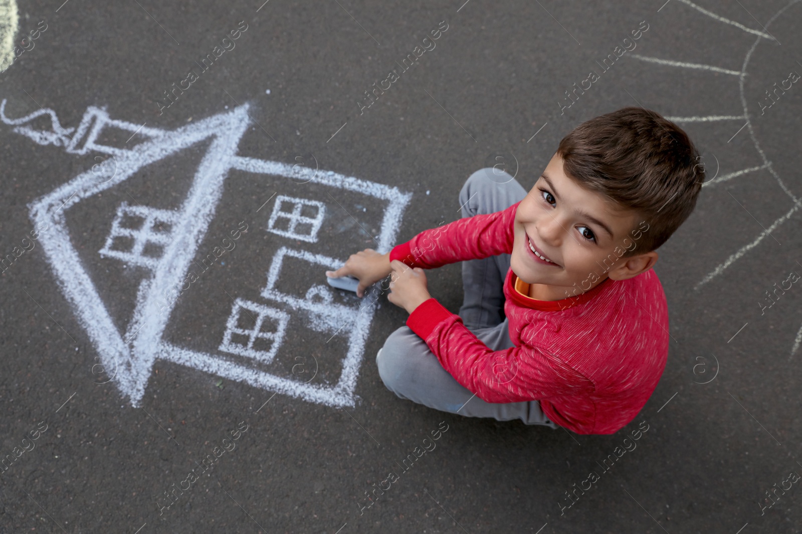 Photo of Child drawing house with chalk on asphalt, above view