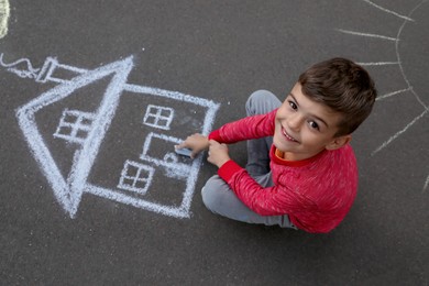 Photo of Child drawing house with chalk on asphalt, above view