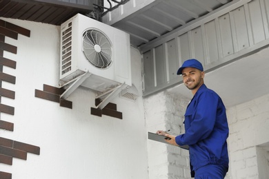 Photo of Professional technician with clipboard near air conditioner outdoors