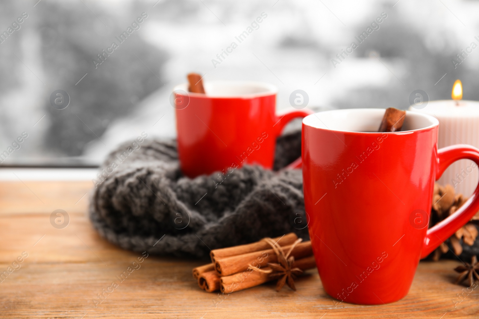 Photo of Cups of hot winter drink with scarf on window sill indoors