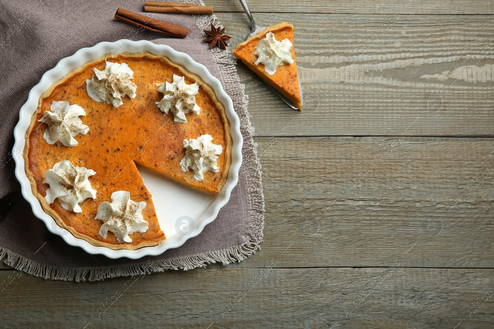 Photo of Delicious pumpkin pie with whipped cream and spices on wooden table, flat lay. Space for text