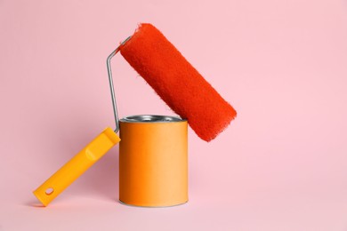 Photo of Can of orange paint and roller on pink background