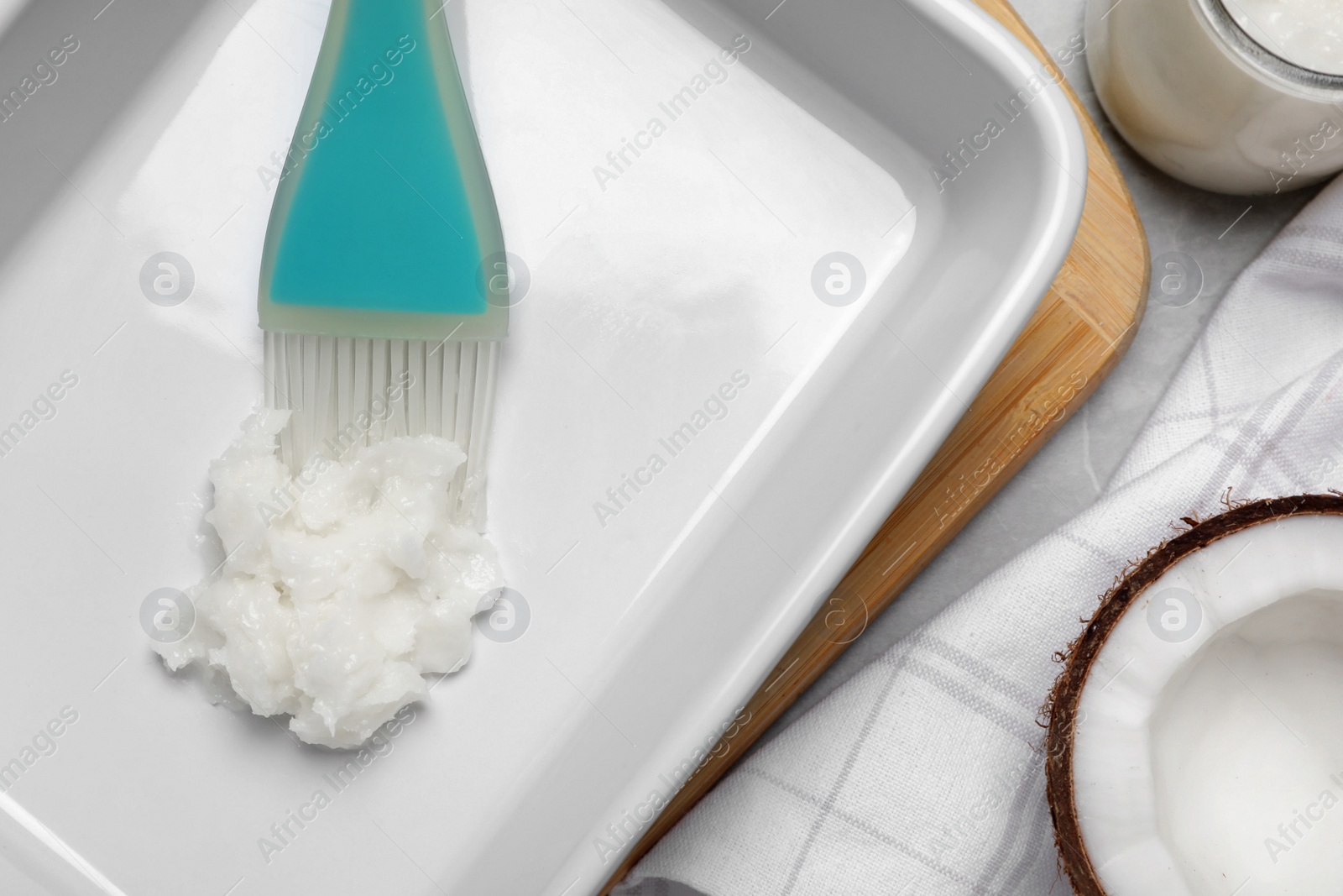 Photo of Baking dish with coconut oil and silicone brush on light grey table, flat lay