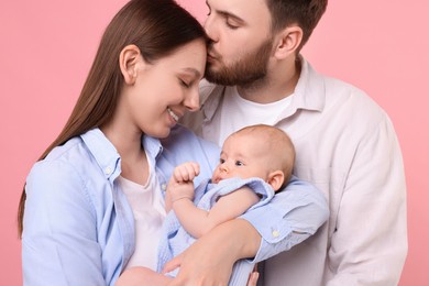 Photo of Happy family. Parents with their cute baby on pink background