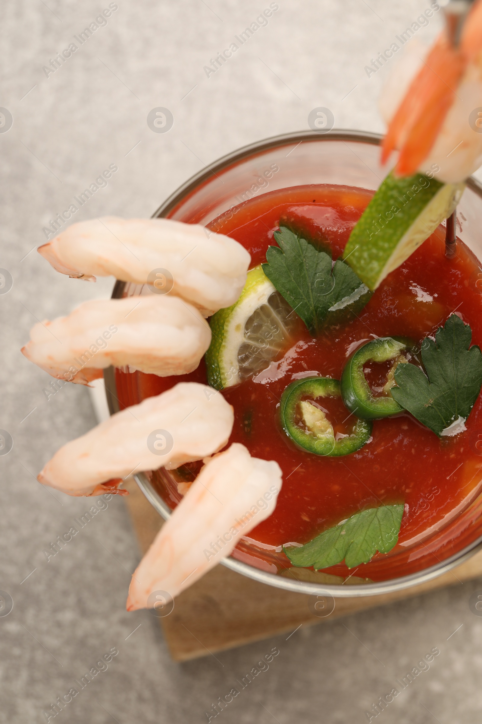 Photo of Tasty shrimp cocktail with sauce, parsley and lime in glass on light grey table, top view