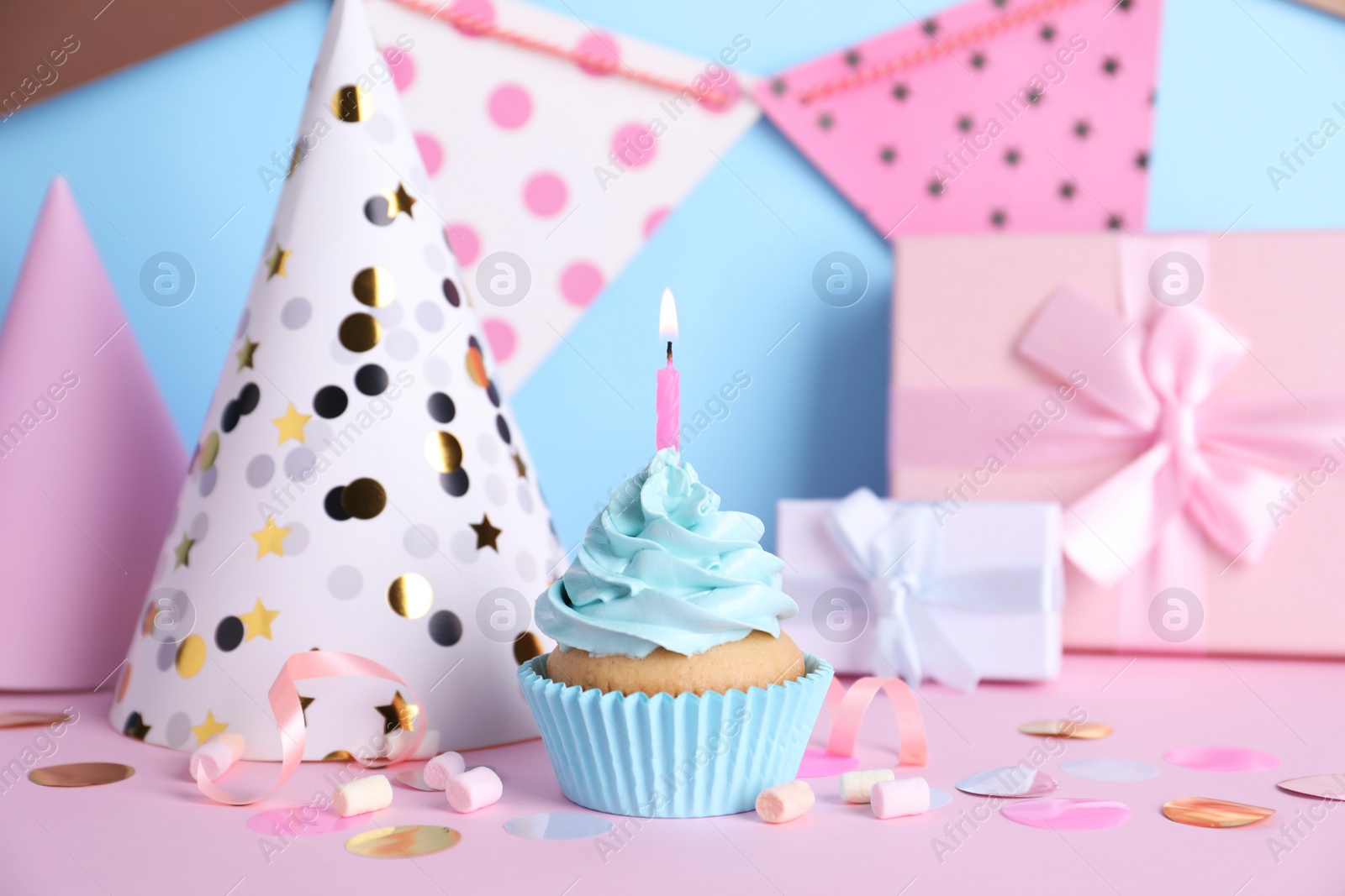 Photo of Delicious birthday cupcake with burning candle, marshmallows and party decor on color background