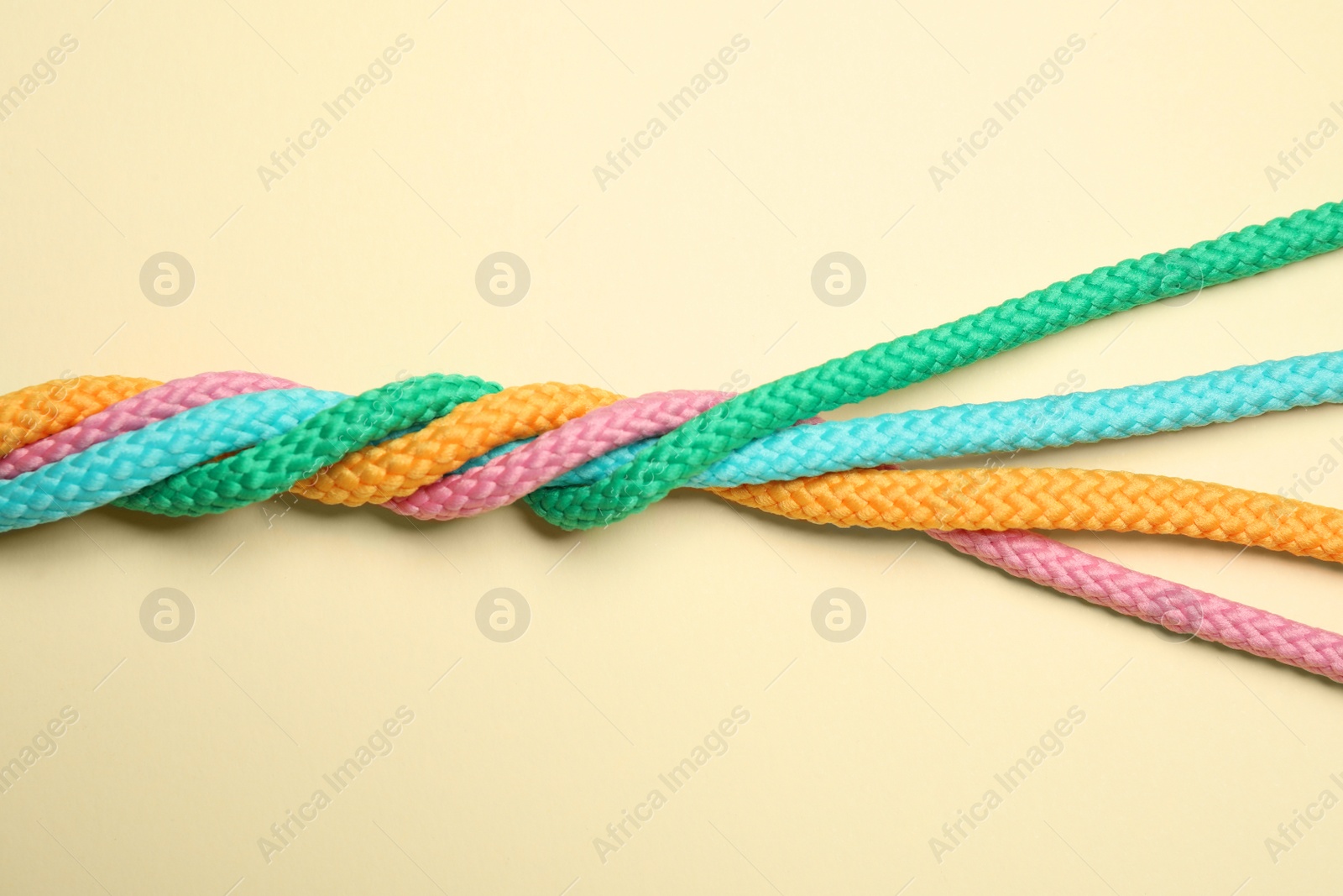 Photo of Twisted colorful ropes on beige background, top view. Unity concept