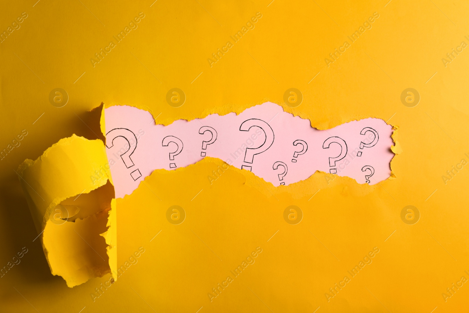 Photo of Question marks on pink background, view through hole in yellow paper