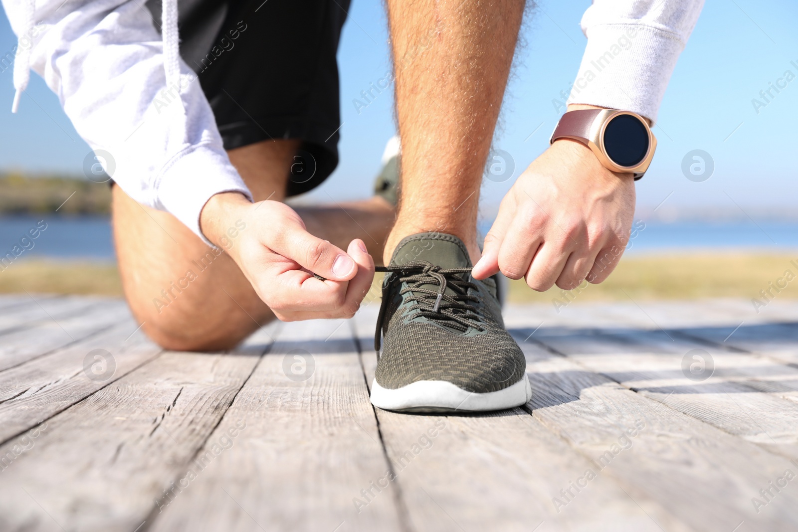 Image of Sporty man tying shoelaces near river on sunny morning, closeup