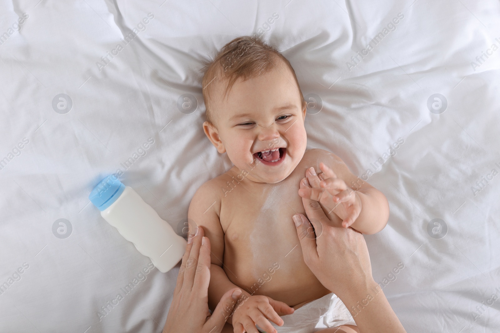 Photo of Mother applying dusting powder onto her baby on bed, top view