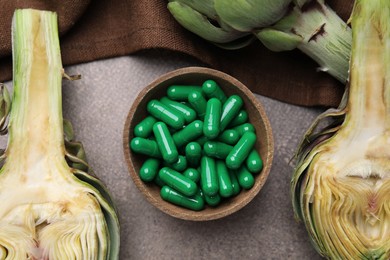 Photo of Bowl with pills and fresh artichokes on brown table, flat lay