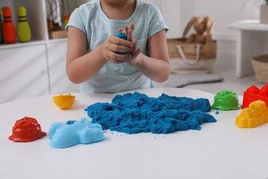 Little boy playing with bright kinetic sand at table indoors, closeup