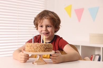 Cute boy with birthday cake at table indoors