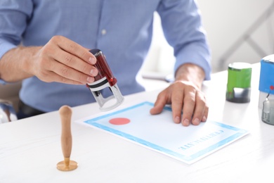 Photo of Male notary stamping document at table in office, closeup