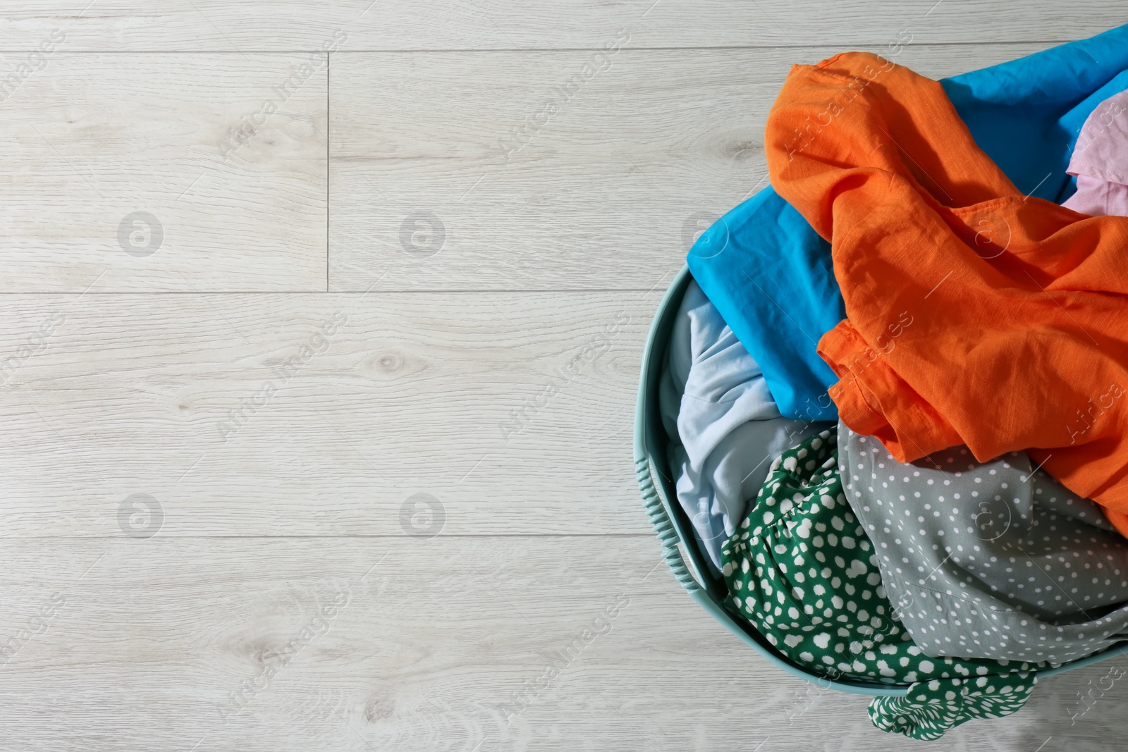 Photo of Laundry basket with clothes on white floor, top view. Space for text