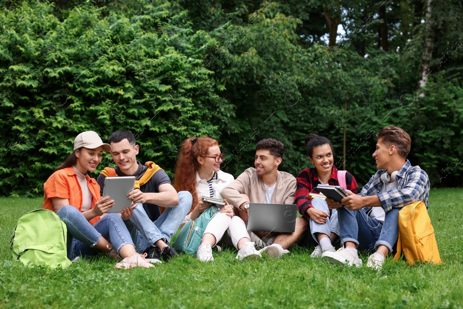 Photo of Group of happy young students learning together on green grass in park
