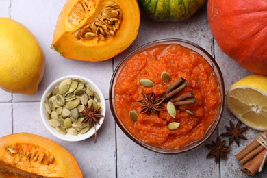 Photo of Bowl of delicious pumpkin jam and ingredients on tiled surface, flat lay