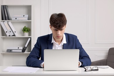 Photo of Young man working at white table in office. Deadline concept