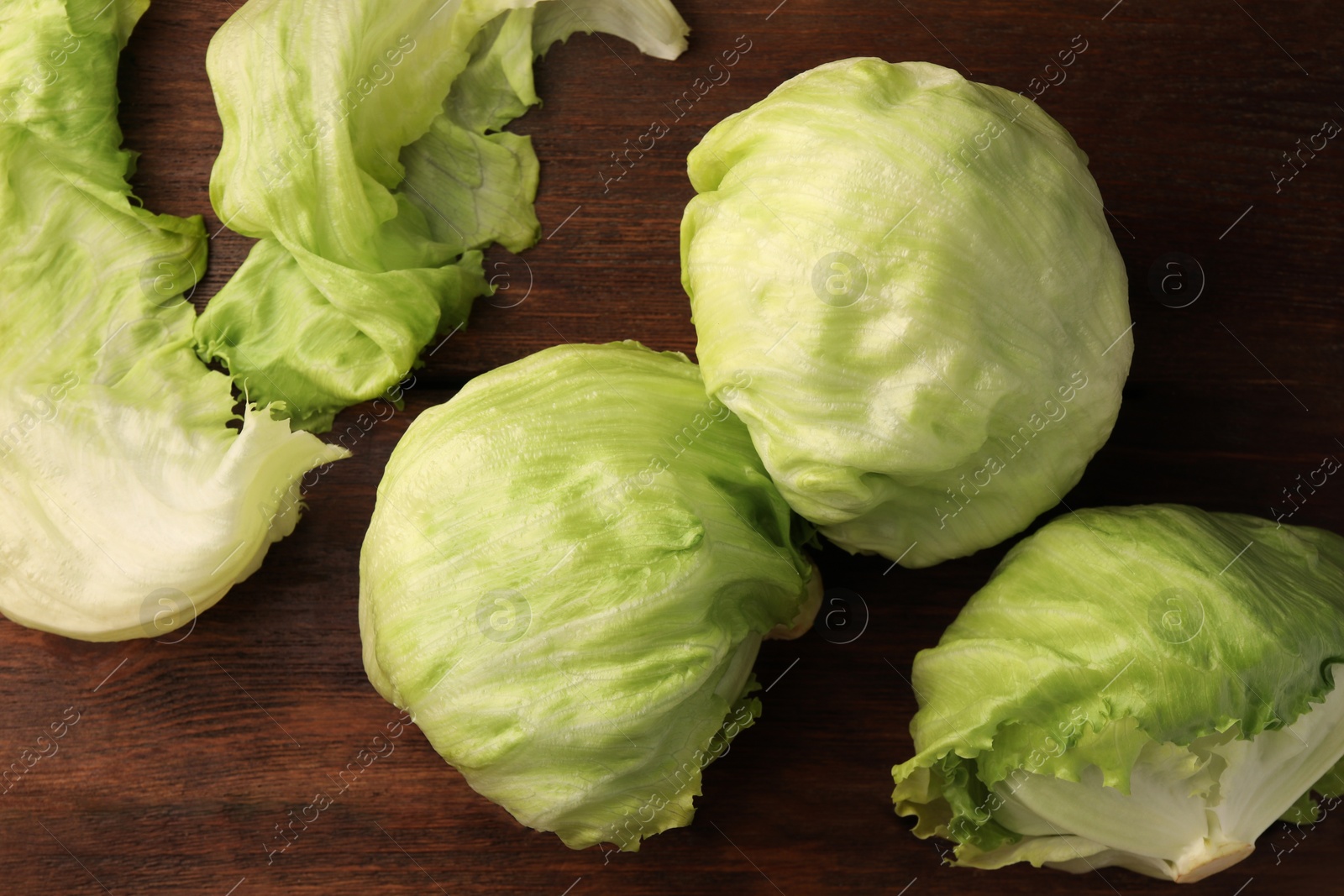 Photo of Fresh green iceberg lettuce heads and leaves on wooden table, flat lay