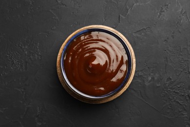 Photo of Tasty barbeque sauce in bowl on dark textured table, top view