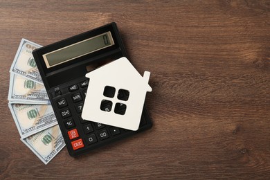Photo of Mortgage concept. House model, calculator and money on wooden table, flat lay with space for text