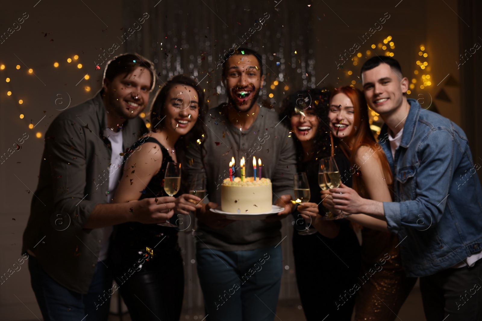 Photo of Happy friends with tasty cake and glasses of sparkling wine celebrating birthday indoors, blurred view