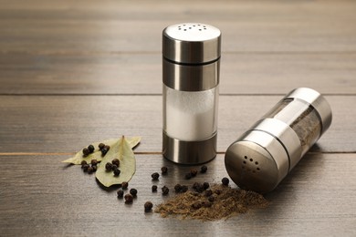 Salt and pepper shakers with bay leaves on wooden table, closeup