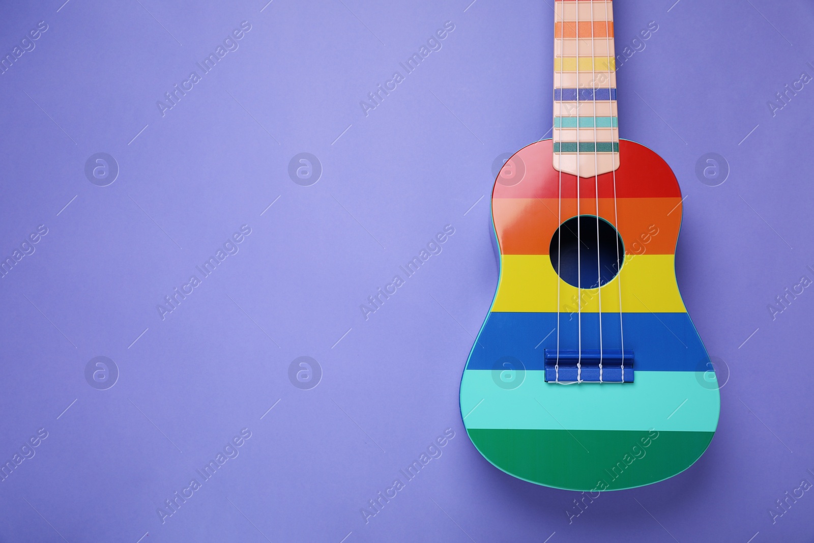 Photo of Colorful ukulele on purple background, top view and space for text. String musical instrument