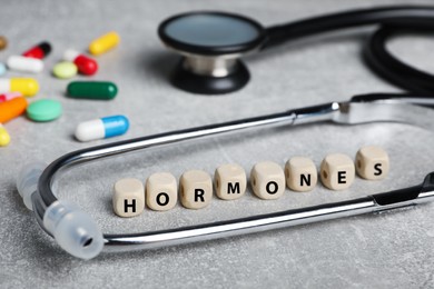 Photo of Word HORMONES made with wooden cubes, stethoscope and pills on grey table, closeup