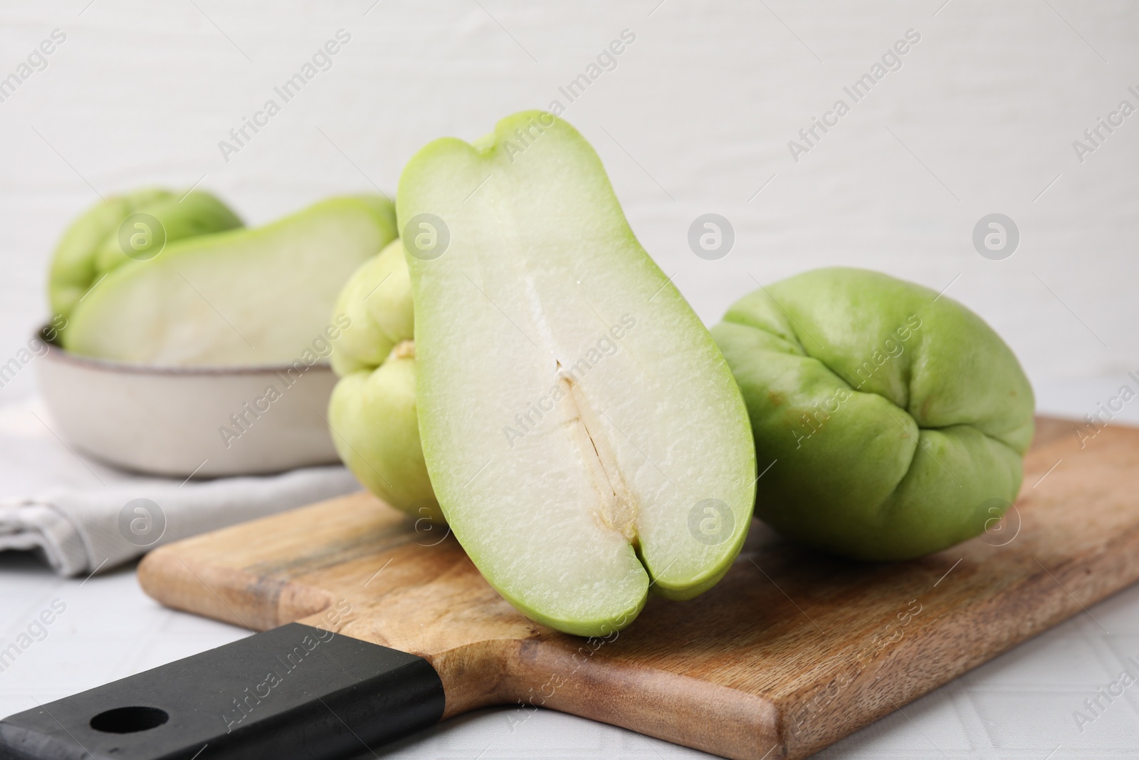 Photo of Cut and whole chayote on white tiled table, closeup