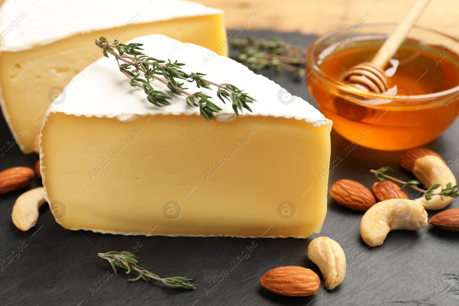 Photo of Tasty Camembert cheese with thyme, honey and nuts on slate plate, closeup