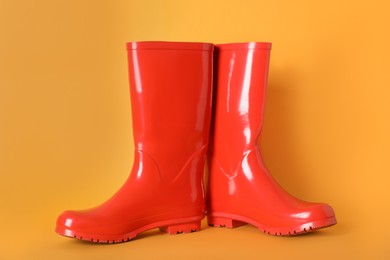 Photo of Pair of red rubber boots on orange background