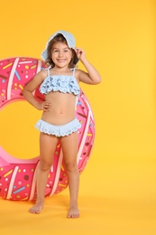 Photo of Cute little child in beachwear with bright inflatable ring on yellow background