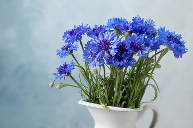 Photo of Bouquet of beautiful cornflowers in vase against light blue background, closeup