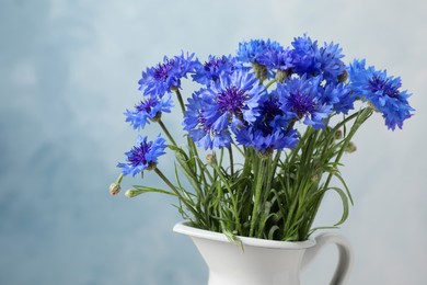 Bouquet of beautiful cornflowers in vase against light blue background, closeup