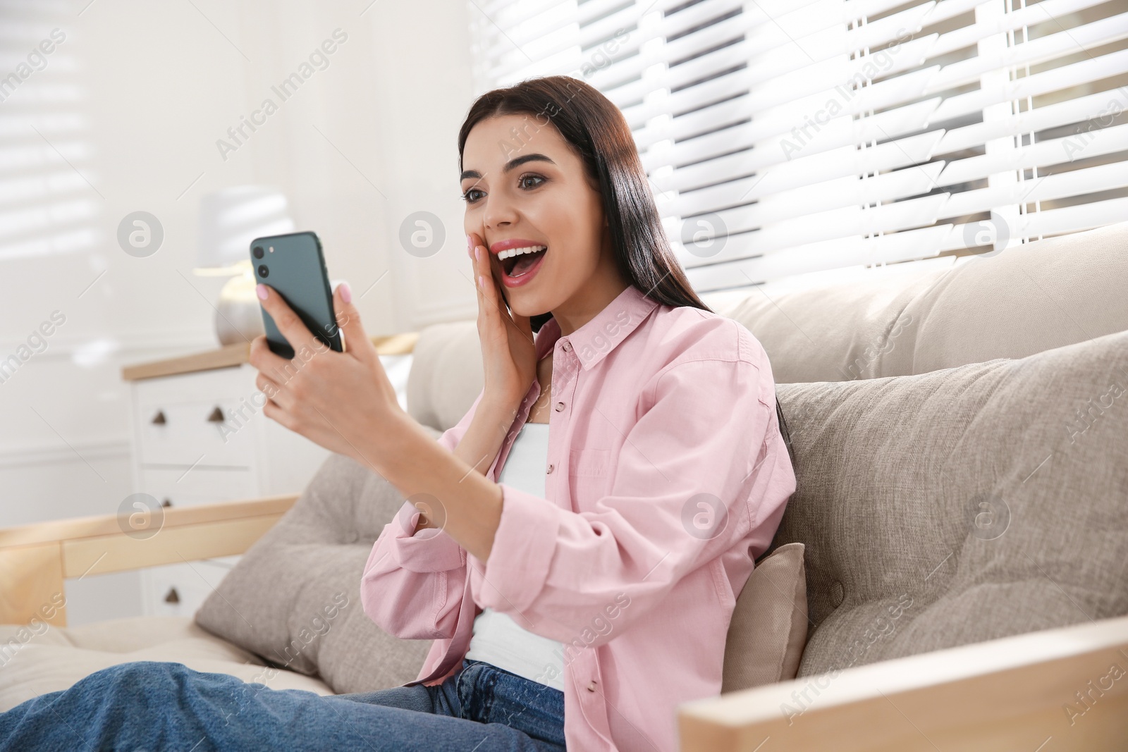 Photo of Emotional woman participating in online auction using smartphone at home