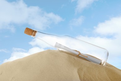 Photo of Corked glass bottle with rolled paper note on sand against sky