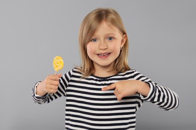 Photo of Portrait of happy girl pointing at lollipop on light grey background